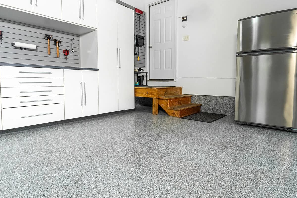 Modern garage interior with grey epoxy floor, storage cabinets, and stainless steel refrigerator.